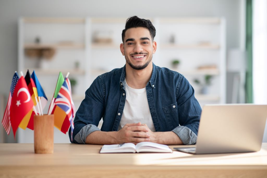 A young man with flags on his desk, working on a laptop